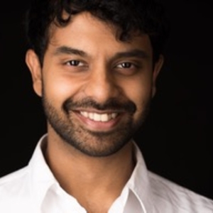Smiling dark-haired person with short beard and white shirt