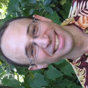 Smiling person in a Hawaiian shirt stands before foliage