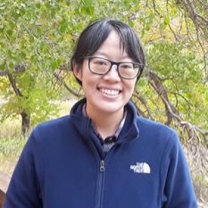 Smiling person with dark bangs in front of a tree