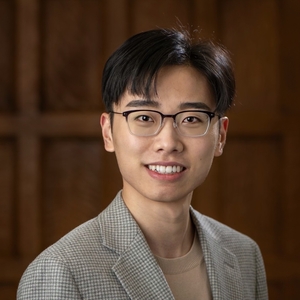 Smiling person with short dark hair wearing glasses and tweed jacket